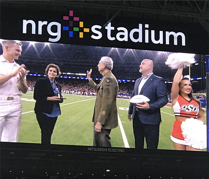 Five people waving to a stadium audience.