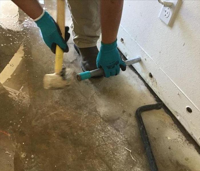 water on the floor of a property, a man making holes in sheetrock to aid in drying process